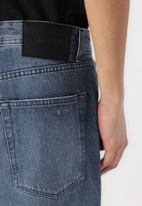 Blå denim jeans med en lett slitt struktur, med et svart lærpatch preget med "ONLY & SONS" på linningen.