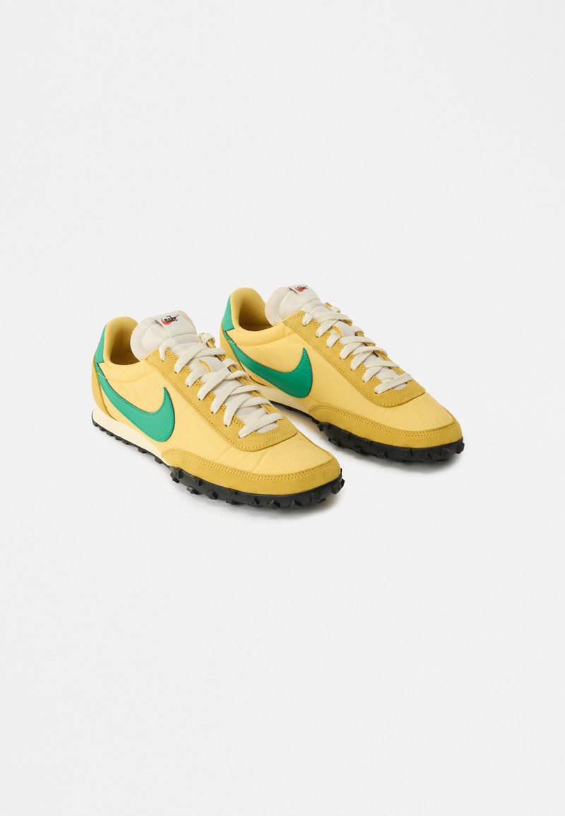 Yellow Nike sneakers with green swoosh logos, white laces, and black textured soles angled to the right on a white background.