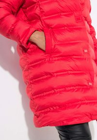 Röd pufferjacka med kviltad design, sidoficka och tryckknappar. Tillverkad av lätt, vattenavvisande material.