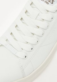 Weiße Ledersneaker mit abgerundetem Zehenbereich, flachen weißen Schnürsenkeln, dezentem Markenlogo und einer strukturierten Lederoberfläche mit minimalen Nähdetails.