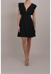 Schwarzes Kleid mit tiefem V-Ausschnitt und gerafften Kurzarmärmeln, ausgestellt Rock, aus glattem Stoff. Sandalen mit goldenen Riemchen ergänzen den Look.