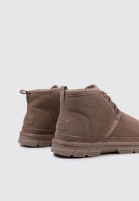 Braune Wildleder-Boots mit runder Zehenpartie, leicht erhöhter Gummisohle, Schnürdesign und dezenten Nahtdetails.