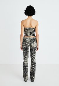 Top sin mangas de estampado negro y beige con detalles fruncidos y pantalones acampanados a juego que presentan un diseño de rayas onduladas y una textura en la tela.