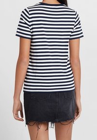 Laivan sininen ja valkoraidallinen lyhythihainen t-paita, jossa on pyöreä pääntie, käytetty mustan farkkuhameen kanssa, jossa on risat reunat ja takataskut.