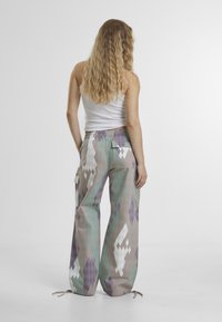 Multicolored patterned cargo pants featuring a loose fit, elastic waistband, and side pockets, with shades of mint green, lavender, and white.
