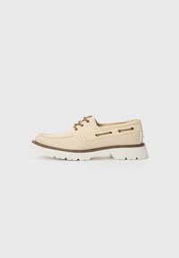 Beige boat shoe with a smooth leather upper, white textured sole, brown accents, and lace-up detailing featuring gold-tone hardware.