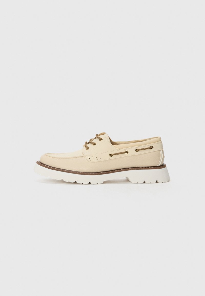 Beige boat shoe with a smooth leather upper, white textured sole, brown accents, and lace-up detailing featuring gold-tone hardware.