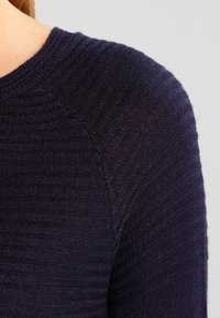 Marinblå stickad tröja med ett strukturerat mönster och horisontella ränder samt rund halsringning, som framhäver det mjuka och lätta tyget.