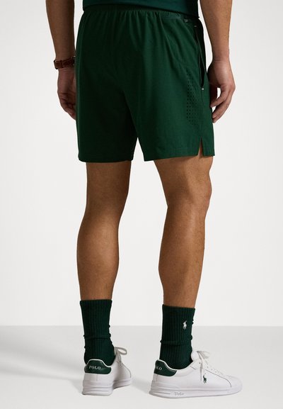 Pantaloni scurți sport verzi cu panouri laterale perforate, talie elastică și o mică fanta la margine. Asortați cu adidași albi și șosete verzi.