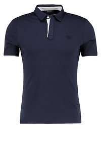 Marinblå pikétröja i mjuk bomull, med vit krage, tvåknappsstfängning och diskret broderad logotyp på bröstet.