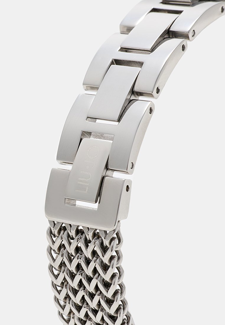 Metalowa bransoleta zegarka z ogniwami połączonymi w sposób interlocking, gładkim, wypolerowanym wykończeniem i plecionym wzorem, głównie w kolorze srebrnym z akcentem markowym.