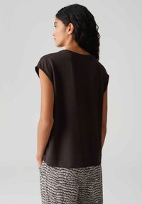 Bruine top met korte mouwen in zachte stof, met een ontspannen pasvorm en een ronde halslijn, gecombineerd met lichte, patroonachtige broek.