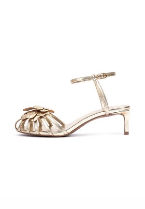 Sandalia dorada de tacón bajo con correa en el tobillo y hebilla, diseño de punta abierta con decoración de flores superpuestas en las correas frontales.