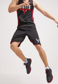 Shorts de basket noirs et maillot sans manches avec des accents rouges, portant un logo des Bulls. Portés avec des chaussures de sport noires et des chaussettes blanches.