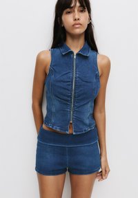 Denim sleeveless top with a collar and front zipper, paired with matching denim high-waisted shorts. Both in a medium blue wash.