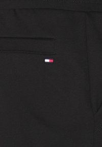 Svart tyg med en horisontell ficka och en liten rektangulär logotyp som har färgerna vit, röd och marinblå nära fickans söm.