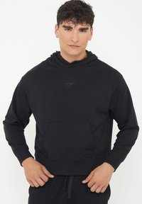 Black hoodie made of soft fabric, featuring a front pocket, hood, and ribbed cuffs. Subtle logo detail stitched on the chest.