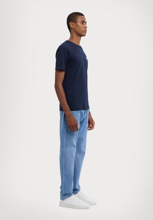 Navy blue short-sleeve t-shirt paired with light blue denim jeans and white sneakers, worn by an individual facing left.