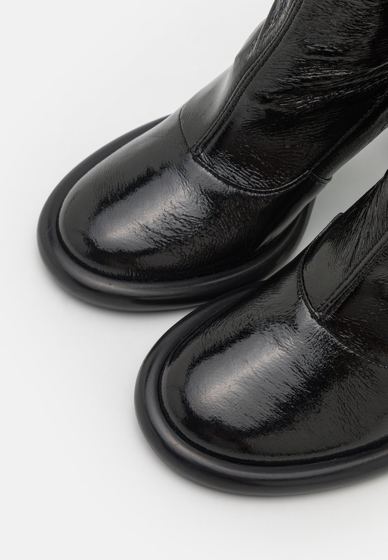 Czarne skórzane botki za kostkę o błyszczącym wykończeniu, zaokrąglonym nosku i płaskiej podeszwie. Minimalistyczny design z gładką fakturą i bez widocznych elementów metalowych.