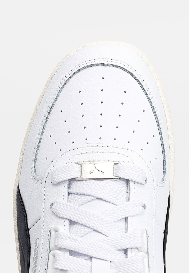 Białe skórzane sneakersy z perforowanym czubkiem, z czarnymi akcentami i srebrnym logo na zaczepie sznurowadeł. Teksturowana powierzchnia i płaskie sznurowadła.