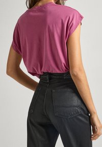 Lila bomulls t-shirt med upprullade ärmar, kombinerad med högmidjade svarta jeans som har bakfickor och en slät yta.