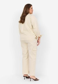 Beige bomullsoutfit i casual stil med en lös skjorta med knapprad och matchande cargobyxor; bärs med svarta klackar i leopardmönster.