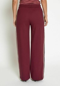 Bordeaux wijde broek met een comfortabele elastische tailleband en contrasterendezijstrepen in crème en zwart. Soepele stoftextuur.
