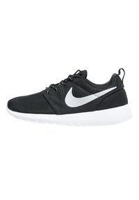 Chaussure de course Nike noire avec logo swoosh blanc, semelle blanche, tige en mesh, lacets noirs et languette au talon, vue de côté sur fond blanc.