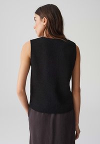 Schwarzes ärmelloses Strickoberteil mit gerippter Textur und geradem Saum, von hinten betrachtet, zeigt ein einfaches, minimalistisches Design.
