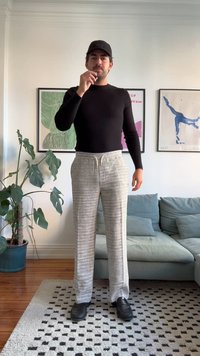 Μαύρη ριμπ μπλούζα με μακριά μανίκια συνδυασμένη με ανοιχτό γκρι σχέδιο παντελόνι φάρδυ. Μαύρα παπούτσια και ένα μαύρο καπέλο συμπληρώνουν την εμφάνιση.