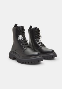 Botas de cuero negro hasta el tobillo con suela gruesa, que presentan un diseño de cordones, cremallera lateral y un adorno de calavera de cristal decorativa.