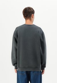 Sudadera gris oscuro de corte relajado, con cuello redondo y mangas amplias. Combinada con pantalones vaqueros azules, mostrando un estilo casual.