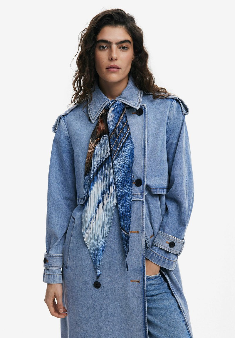 Dunkelblauer Denim-Trenchcoat mit Kragen, langen Ärmeln und zwei Fronttaschen. Mit einem blauen gemusterten Schal, der um den Hals gebunden ist.