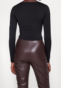 Svart långärmad topp med en figurnära design, kombinerad med högmidjade, glänsande bruna fusk läderbyxor. Slät textur med en cropped stil.