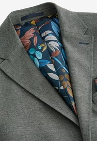 Grau strukturiertes Blazer mit einer floral gemusterten marineblauen Innenauskleidung, die Blätter in verschiedenen Farben zeigt. Auffälliges Reversdesign.