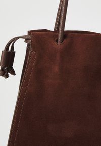 Rucsac din piele întoarsă maro cu accente din piele netedă, având o formă rotundă și un finisaj texturat, evidențiind măiestria și calitatea.