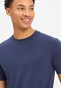 Granatowa bawełniana koszulka z okrągłym dekoltem, krótkimi rękawami, gładką teksturą i minimalną ilością szwów; prezentowana na uśmiechniętym modelu.