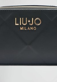 Crni novčanik od umjetne kože s kvadratnim uzorkom, zlatnim hardverom s utisnutim "LIU·JO MILANO" i zatvaranjem na munju na vrhu.
