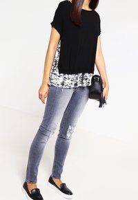 Mustavalkoinen kerroksellinen t-paita lyhyillä hihoilla, yhdistettynä haalistuneisiin harmaisiin skinny-farkkuihin, joissa on kulutusta ja mustat slip-on kengät.