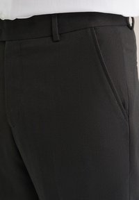 Fekete halszálkás mintázatú nadrág, sima textúrával, oldalsó zsebbel és övcsattal ellátott derékkal.