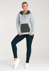 Szara bluza z kapturem z ciemnoszarym teksturowanym kieszeniem, z regulowanym kapturem w jasnoszarym kolorze, zestawiona z ciemnymi dżinsami i białymi trampkami.