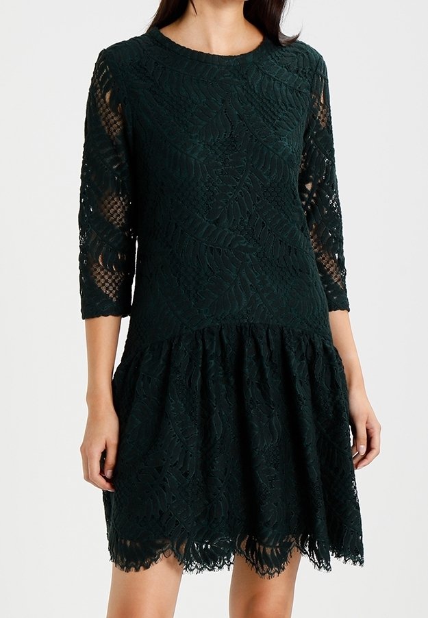 Dunkelgrünes Spitzenkleid mit Dreiviertelärmeln, floralem Muster und schwingendem Saum. Aufwendige Spitzenstruktur mit gewelltem Rand.