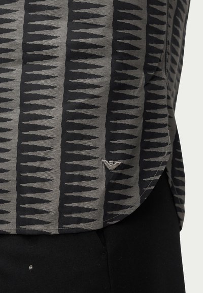 Μαύρο και γκρι ριγέ πουκάμισο με κάθετες οδοντωτές γραμμές, συνδυασμένο με μαύρο παντελόνι.