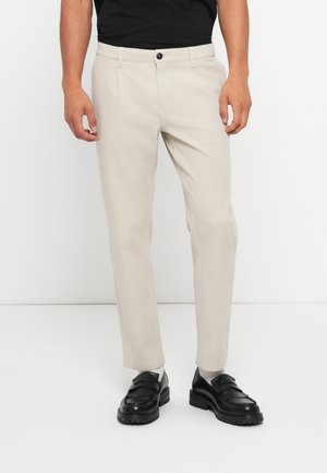 Beige cotton pants with a straight cut, featuring front pockets and a single button closure. Paired with black loafers.