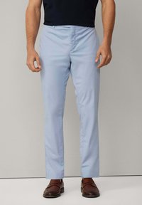 Ljusblå dressbyxor med rak benutskrift, slät textur och standard framtill; matchas med bruna läderskor.