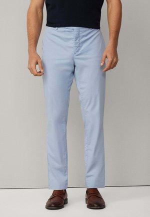 Hellblaue Stoffhose mit geradem Bein, glatter Textur und klassischem Verschluss vorne; kombiniert mit braunen Lederschuhen.