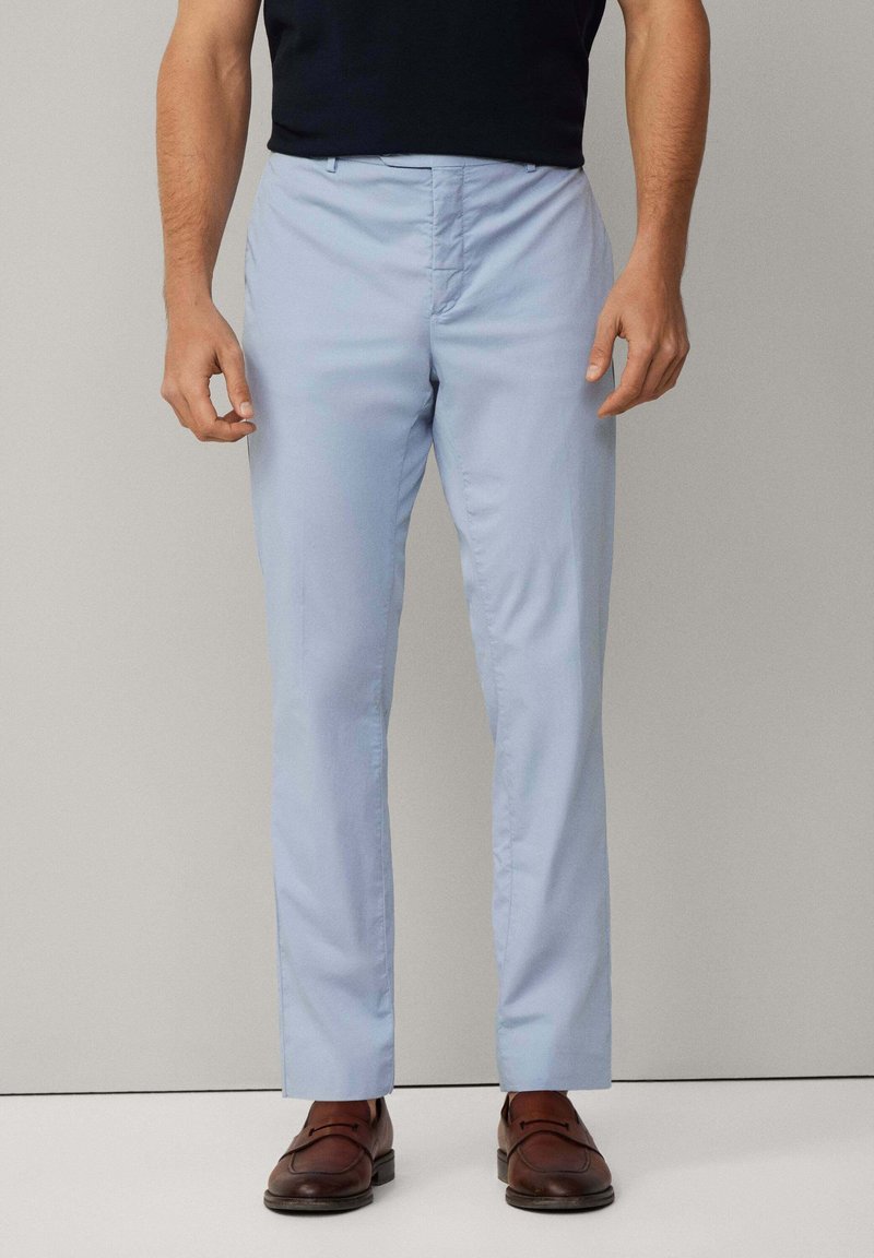 Ljusblå dressbyxor med rak benutskrift, slät textur och standard framtill; matchas med bruna läderskor.