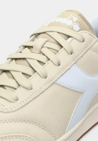 Ανοιχτό μπεζ αθλητικά παπούτσια από σουέντ με επίπεδα μπεζ κορδόνια. Διαθέτουν ανοιχτή μπλε λεπτομέρεια και υφασμένο λαστιχένιο πάτο. Λογότυπο στη γλώσσα.