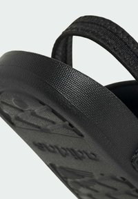 Musta sandaali, jossa on tekstuurilla varustettu kumipohja. Sandaalissa on leveä hihna mattapinnalla ja hillitty logo painettuna pohjaan.