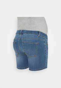 Pantalones cortos de maternidad de denim con bolsillos traseros y un panel elástico de tejido gris para soporte del vientre sobre un fondo liso.